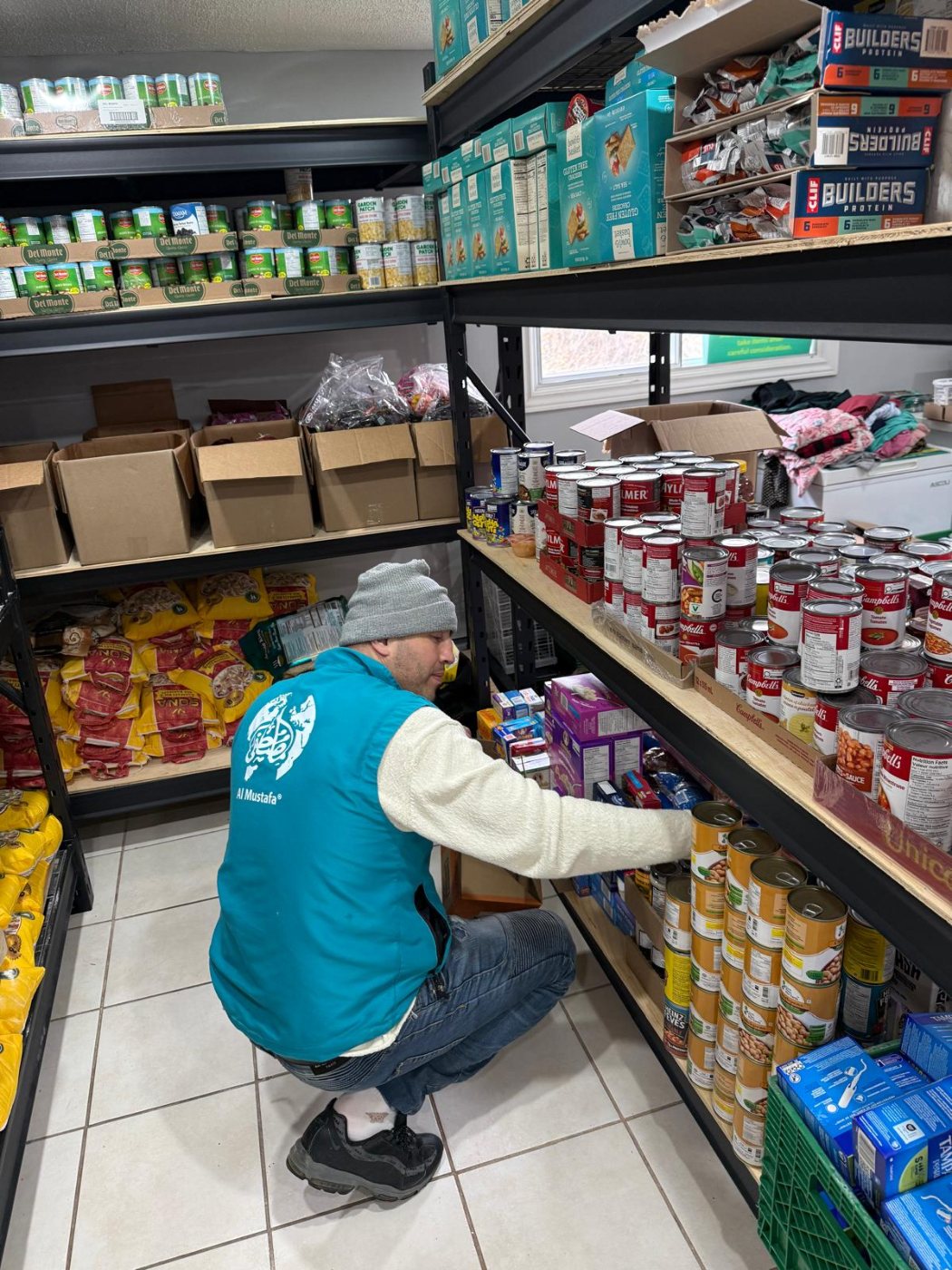 A volunteer crouching to restock tinned goods on a food bank shelf