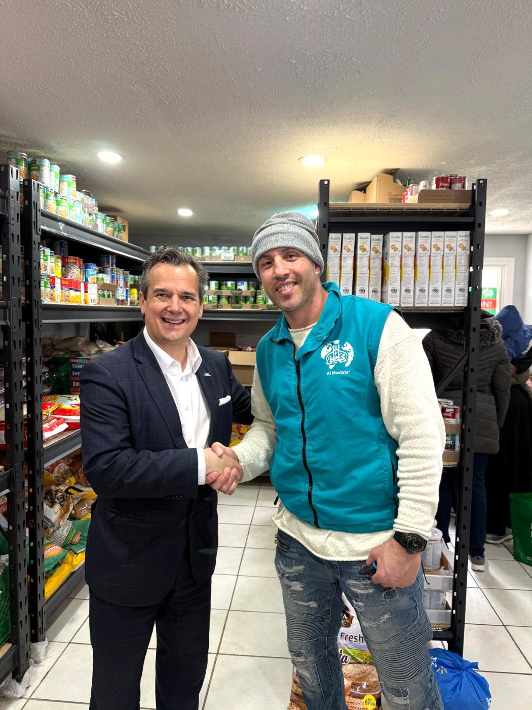 A volunteer shaking hands with a visitor among the food bank shelves