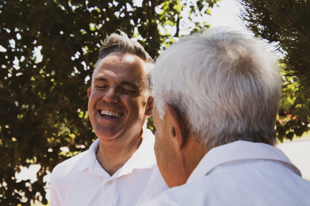 Two older men laughing together outdoors on a sunny day